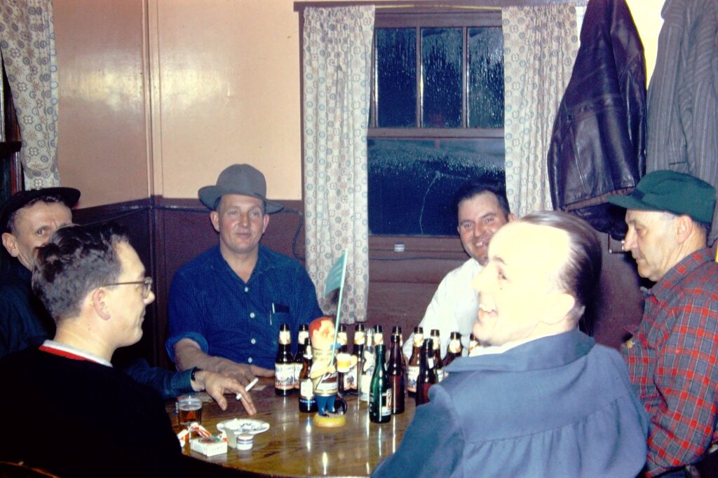Group of men around a round table next to window, beer bottles, smoking